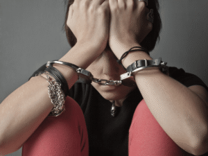 A distressed young person sits with their head in their hands while wearing handcuffs. Image represents Colorado juvenile criminal defense, youth offender rights, and the need for legal representation for minors.