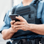 Police officer in a tactical vest using a smartphone, symbolizing the legal question of whether police search phone without warrant Colorado is allowed.