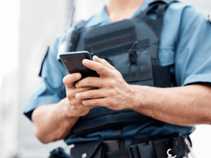 Police officer in a tactical vest using a smartphone, symbolizing the legal question of whether police search phone without warrant Colorado is allowed.