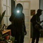 Two masked intruders breaking into a home at night with a flashlight, symbolizing the crime that leads to conspiracy to commit theft Colorado charges.